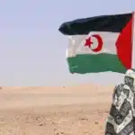 امرأة صحراوية ترتدي ملحفة تقف في الصحراء وترفع علم الجمهورية الصحراوية