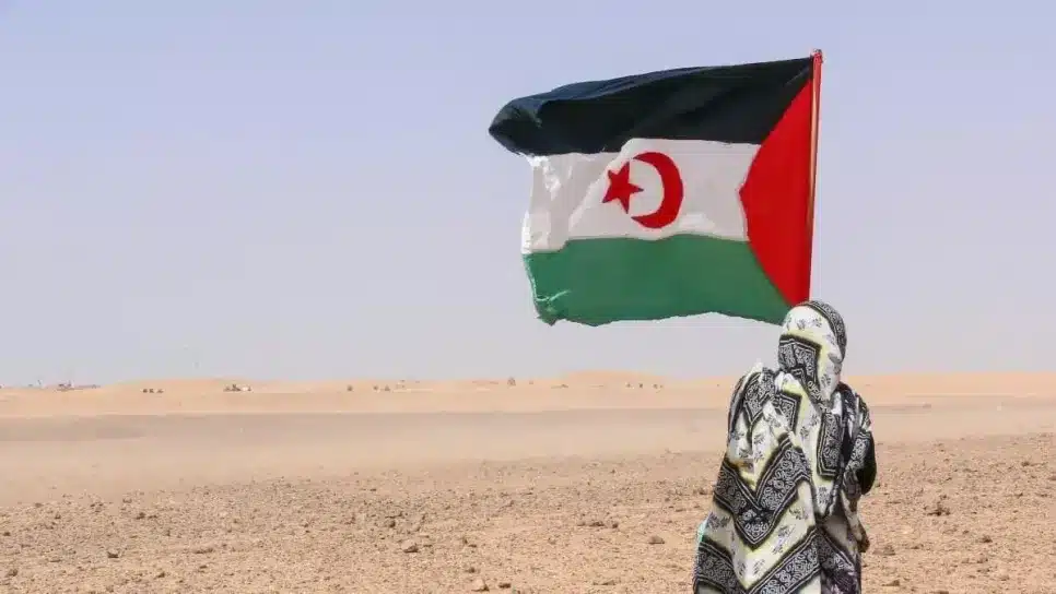 امرأة صحراوية ترتدي ملحفة تقف في الصحراء وترفع علم الجمهورية الصحراوية